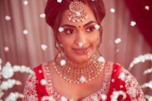 A beautiful Indian bride in traditional jewelry peeks coyly through a decorative veil.