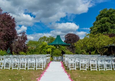 Outdoor wedding setup with white chairs and aisle under blue sky and green canopy.
