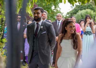Bride and groom smiling while standing before guests during wedding ceremony.