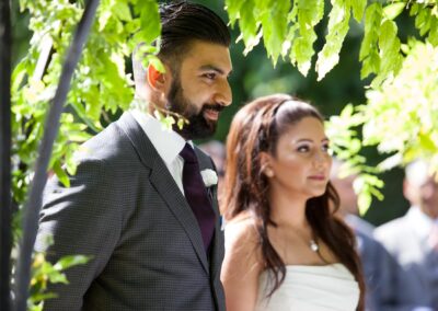 Bride and groom standing together under green leaves during ceremony.