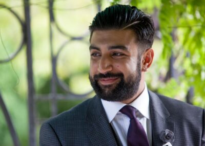 Groom smiling warmly under green arch during outdoor wedding ceremony.