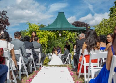 Outdoor wedding ceremony view with guests seated and couple under green canopy.