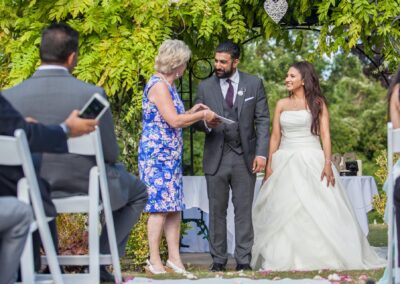 Bride and groom standing with officiant under floral arch during ceremony.