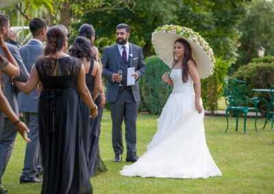 Bride holding floral parasol and talking with guests on the garden lawn.