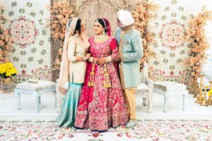 An Indian bride and groom with a guest stand in a beautifully decorated room.