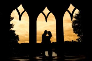A silhouetted couple kisses through an arched window at sunset.