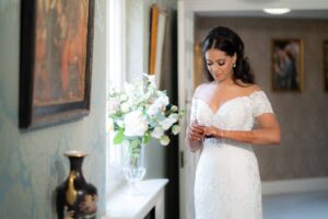 A beautiful bride in a white gown adjusts jewelry, showing intricate mehndi.