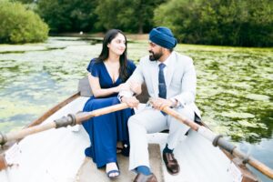 A man and woman in a rowboat on a lily pad-covered lake, looking at each other.