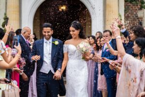 A joyful bride and groom walk through falling confetti after their wedding.