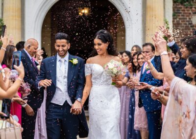 A joyful bride and groom walk through falling confetti after their wedding.