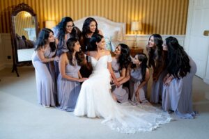 A bride sits surrounded by her bridesmaids in a warm, intimate room.