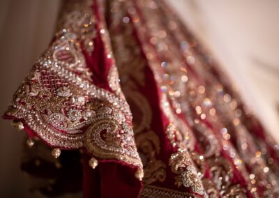 Close-up of embroidered maroon bridal lehenga with intricate gold beadwork detail.