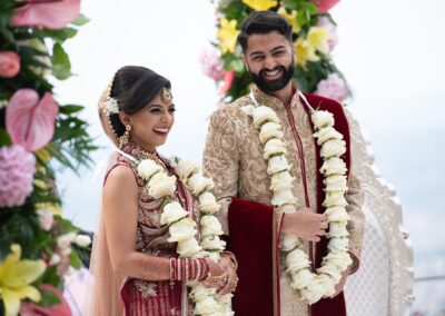 Bride and groom smiling joyfully during Hindu wedding ceremony outdoors.
