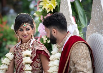 Bride smiling at groom while seated during wedding ceremony under flower arch.