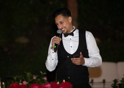 Man in black waistcoat giving a lively wedding speech with a microphone.