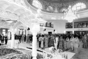 A black and white photo of a large Indian wedding ceremony indoors.