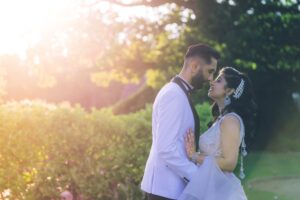 A bride and groom share a tender moment with sun flare in a garden.