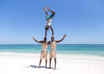 Three acrobatic men in traditional attire form a human tower on a sunny beach.
