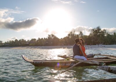 A couple shares a tender moment on a traditional wooden boat in sunlit tropical waters.