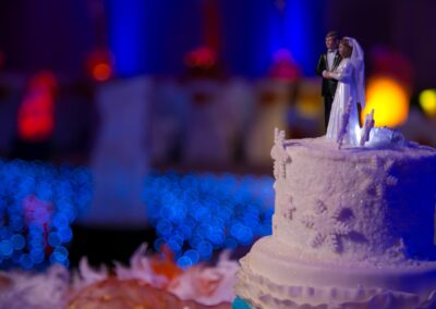 Close-up of white wedding cake with bride and groom figurine topper and lights.