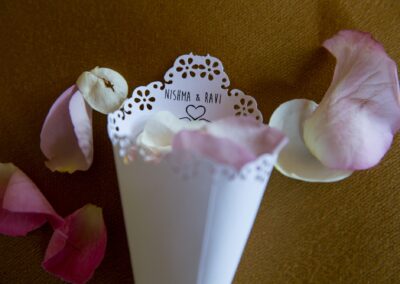 A paper cone with "NISHMA & RAVI" surrounded by pink and white rose petals.