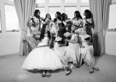 Black and white photo of the bride and bridesmaids posing by large windows.