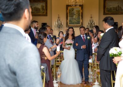 The bride, holding a pink bouquet, walks down the aisle with her father.