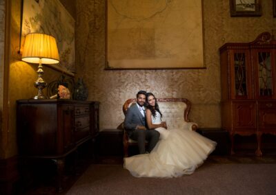 A bride and groom sit together on an ornate sofa in a richly decorated room.