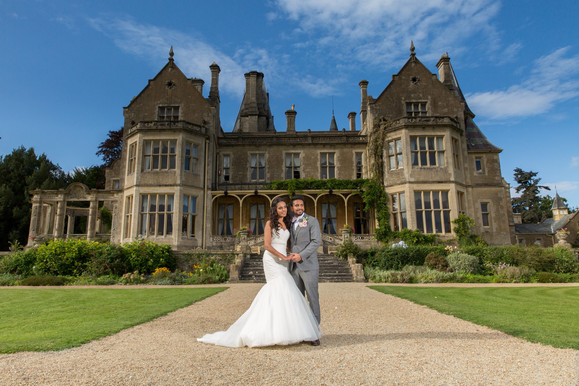 destination-wedding-orchardleigh-estate-nishma-ravi-16 A newlywed couple, radiant, stands on a gravel path leading to a stately manor.