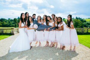 Bridesmaids lift the groom in a playful outdoor wedding photo.