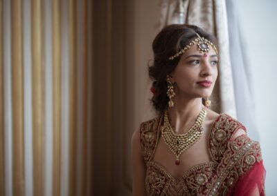 A beautiful Indian bride in traditional attire, adorned with intricate jewelry, looking out.