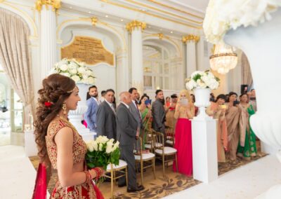 An Indian bride, holding a bouquet, smiles as she walks past guests at her wedding ceremony.