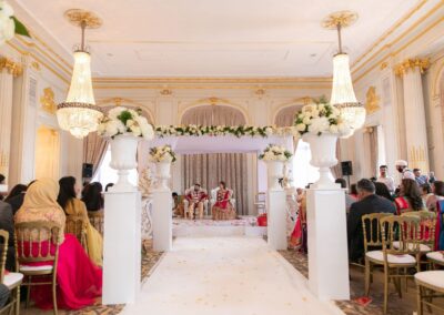 A wide shot of an Indian wedding ceremony venue, with the bride and groom seated under a mandap.