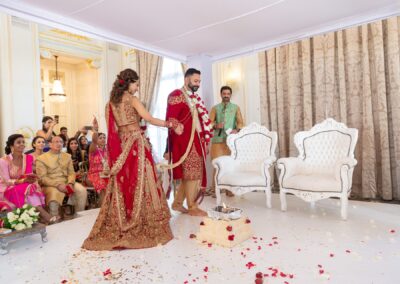 An Indian bride and groom stand holding hands at their wedding ceremony, surrounded by guests.