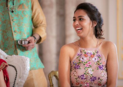 A young woman in a floral top laughs joyfully at an Indian wedding ceremony.