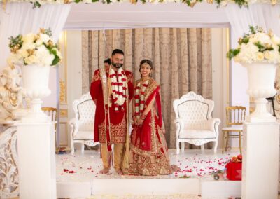 The bride and groom, adorned with flower garlands, stand at their wedding altar.