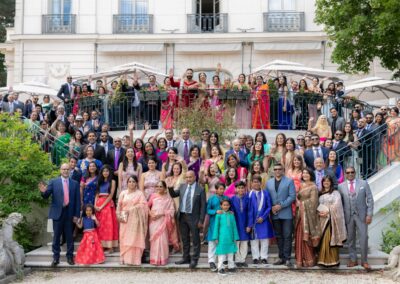 A large wedding party waves on the steps of a grand building.