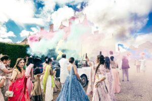 Wedding guests release colorful smoke bombs around a convertible car.