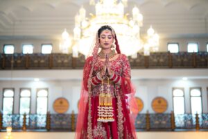 A bride in a red and gold dress prays under a large chandelier.