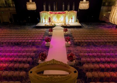An aerial view of a grand wedding hall, showcasing the mandap, aisle, and rows of chairs.