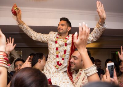 An Indian groom is carried on shoulders, cheering with hands raised amidst excited crowd.