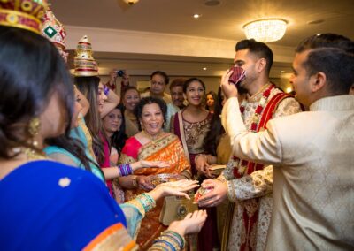 A laughing groom participates in a playful ritual, surrounded by smiling guests.