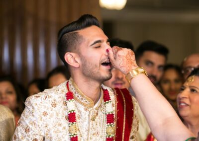 A hand gently touches the groom's nose as he smiles, during a ceremony.