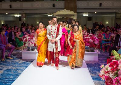 A groom walks down the aisle with two women, surrounded by guests.
