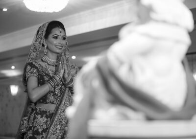 A bride in traditional attire with hands clasped in prayer, in black and white.