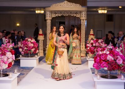 Three women in traditional dresses walk down a petal-strewn aisle.