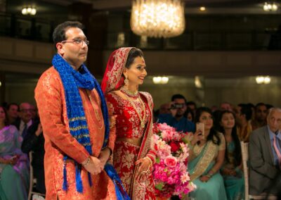 A bride and a man in traditional attire stand smiling at a wedding ceremony.