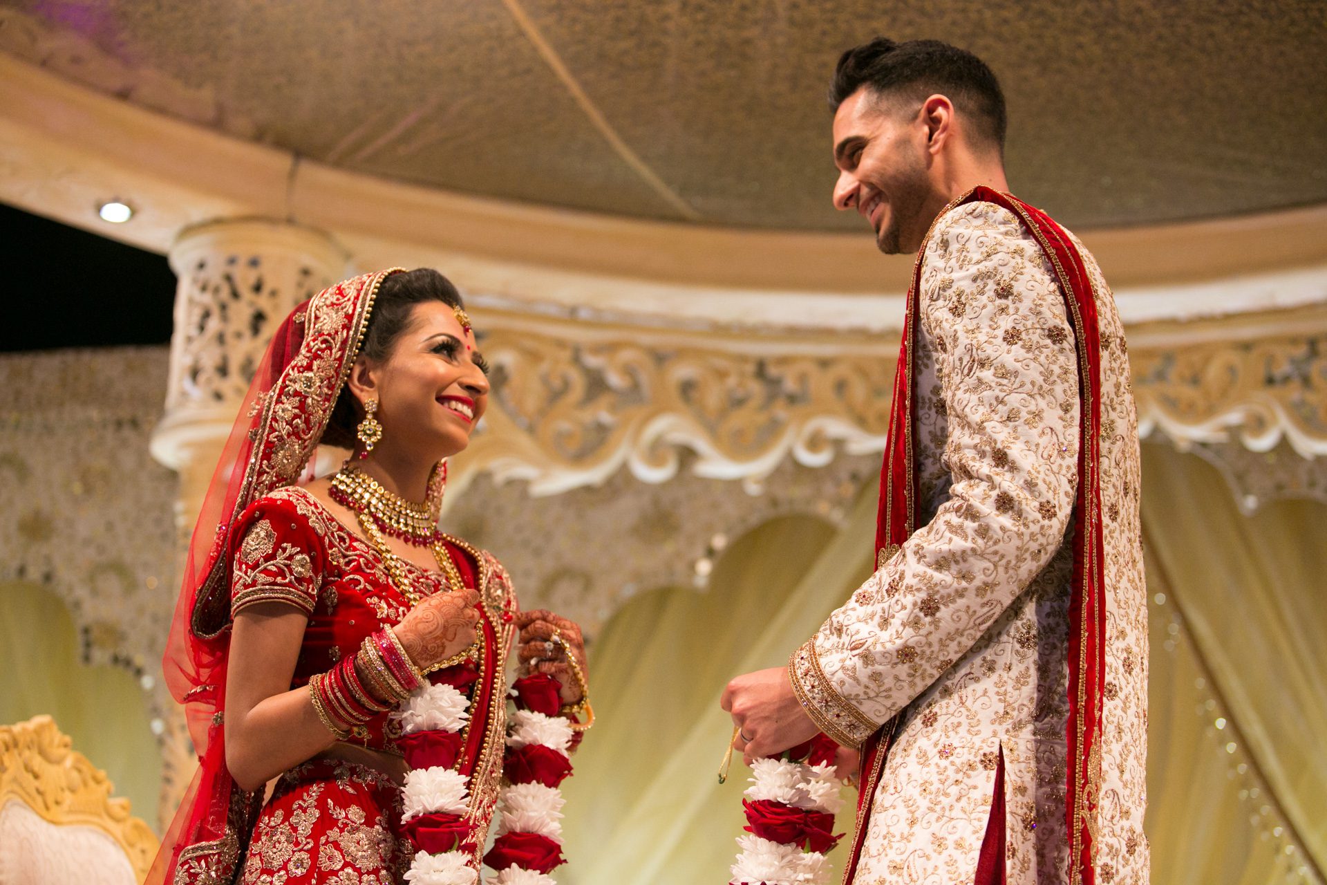 hindu-wedding-grosvenor-house-payal-neel-22 A bride and groom smile at each other, holding garlands during a ceremony.