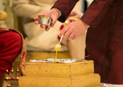 A person pours a yellow liquid from a spoon onto a ceremonial fire altar.