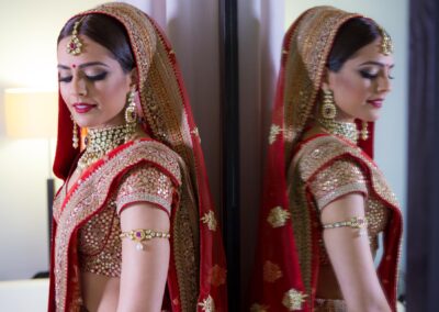 Bride in red lehenga reflected in mirror before Hindu wedding ceremony.